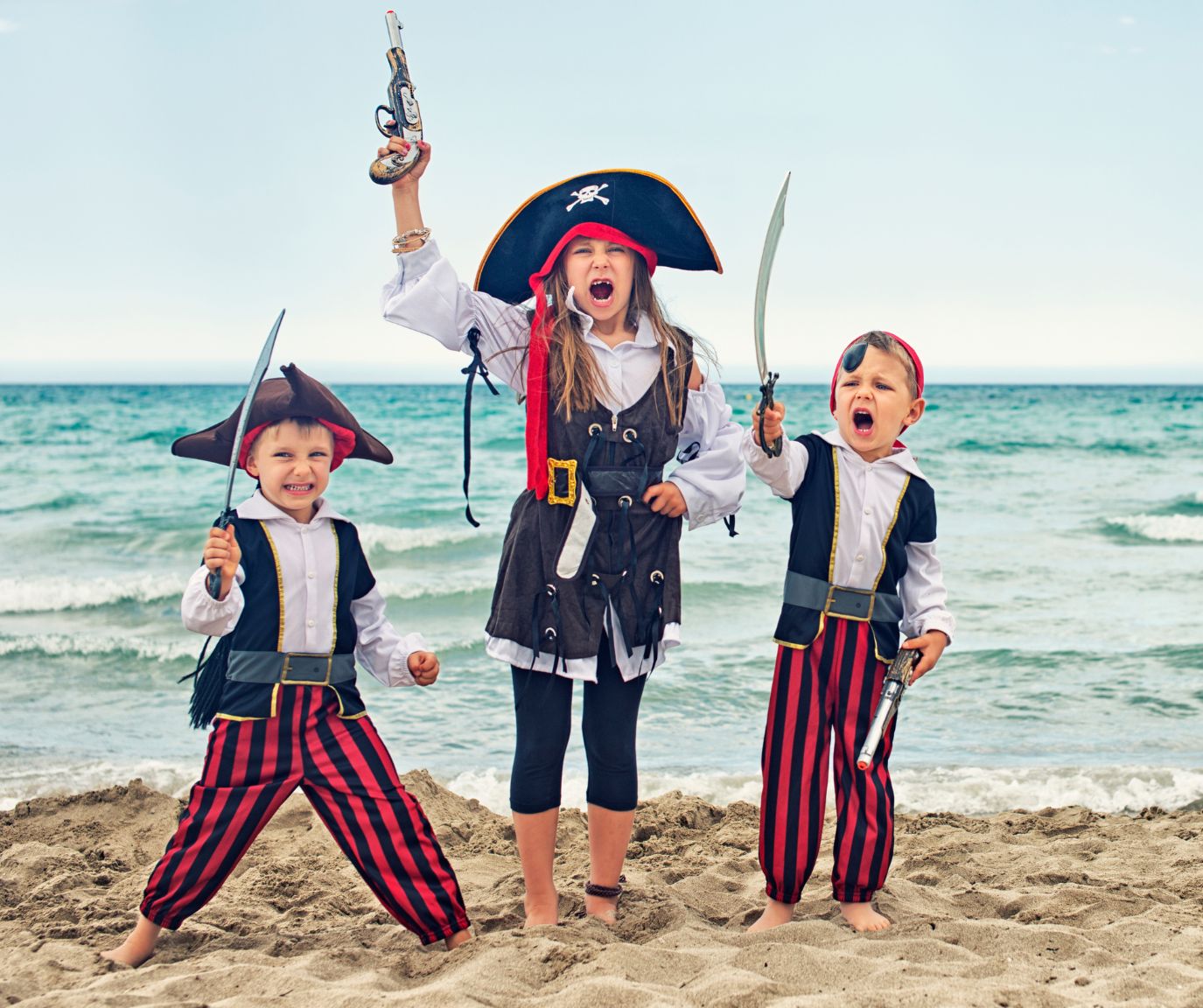 tre bambini giocano in spiaggia vestiti da pirati